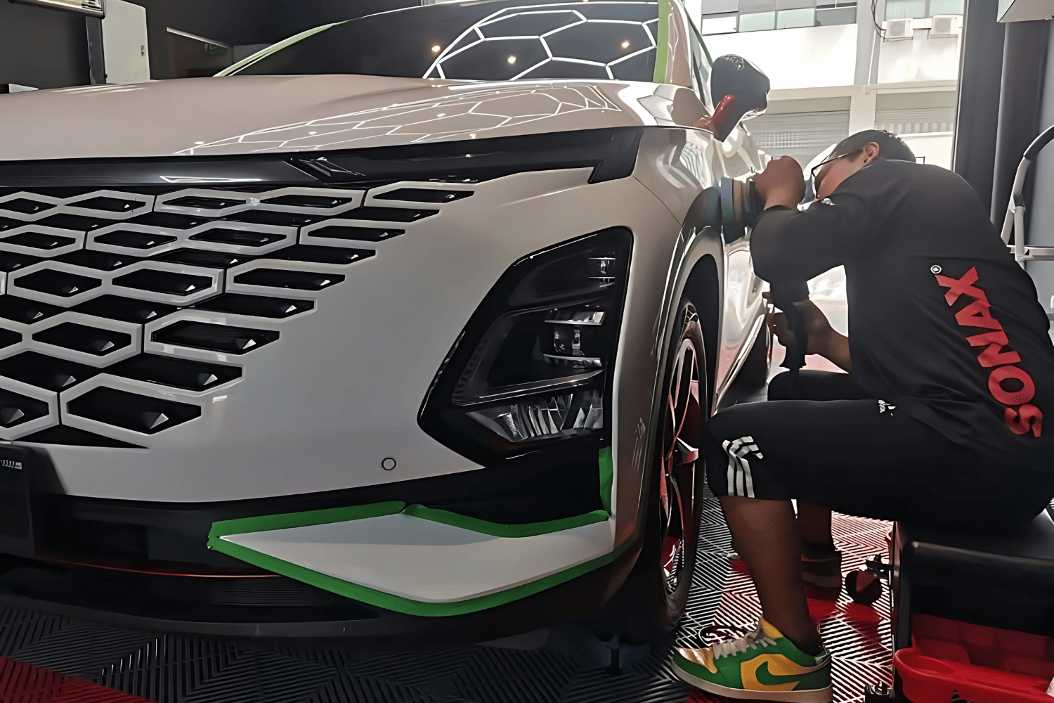 Detailing Valet technician polishing a white Chery Omoda 5 SUV inside the studio with hexagon lights reflecting on the hood